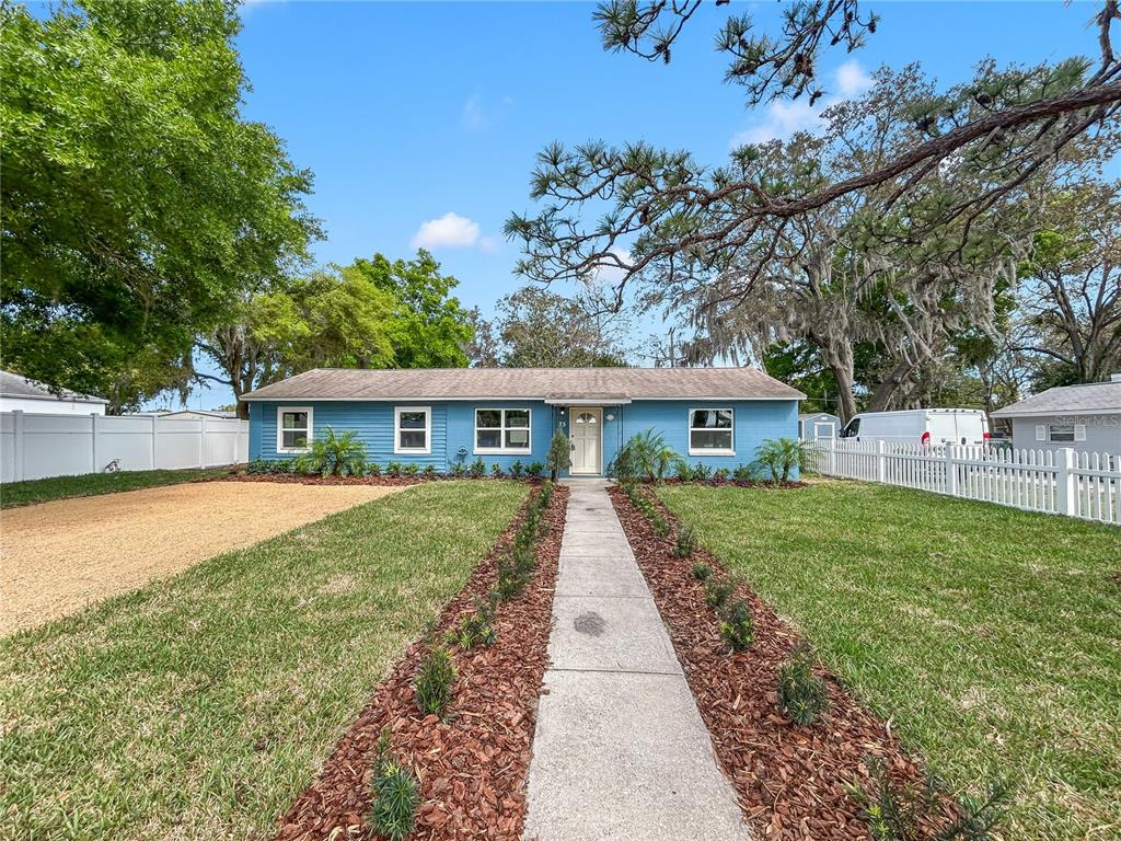 A blue single-story house with a gravel driveway and a concrete walkway leading to the entrance — 25 E CHARLOTTE AVENUE, EUSTIS, FL