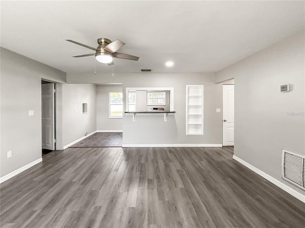 A living room with gray wood-look flooring, a ceiling fan, and a kitchen pass-through window — 25 E CHARLOTTE AVENUE, EUSTIS, FL