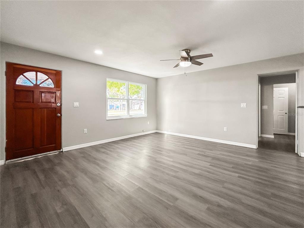 An empty living room features gray wood-look flooring, light gray walls, and a ceiling fan — 25 E CHARLOTTE AVENUE, EUSTIS, FL