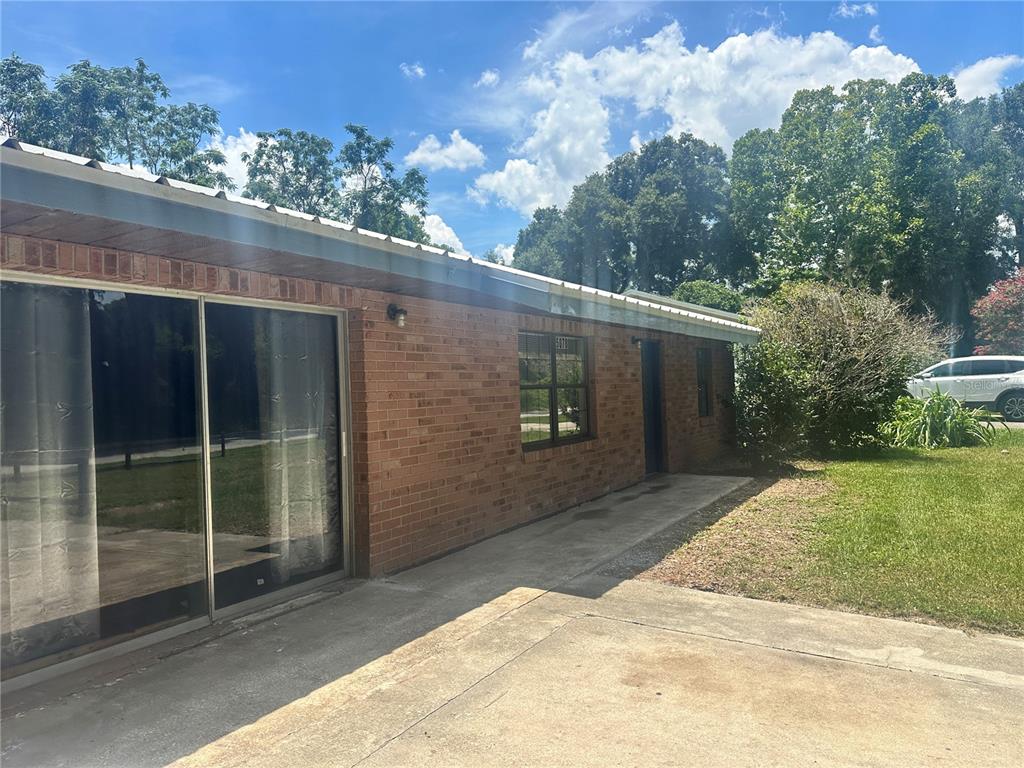 A brick house exterior features a sliding glass door, a window, and a concrete patio — 5078 SE 135TH STREET, SUMMERFIELD, FL