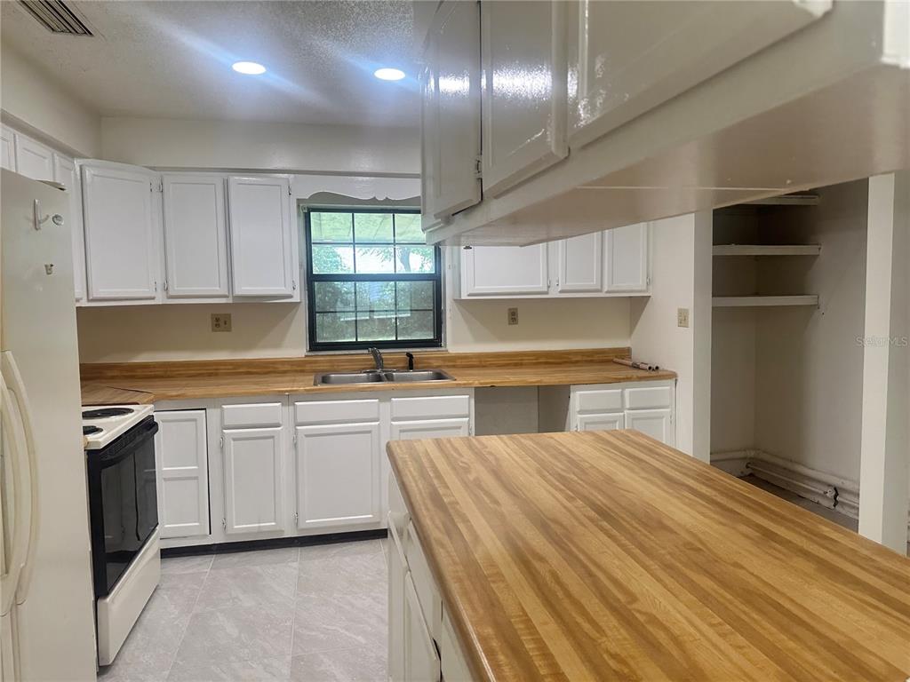 A kitchen features white cabinets, wood-look laminate countertops, a window, and a central island — 5078 SE 135TH STREET, SUMMERFIELD, FL