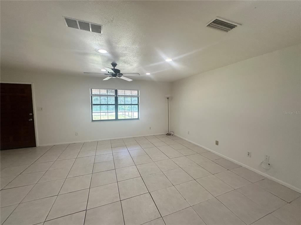 An empty living room features white walls, light-colored tile flooring, a ceiling fan, and a window — 5078 SE 135TH STREET, SUMMERFIELD, FL
