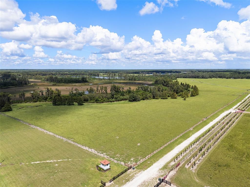 An aerial view shows a large, fenced green pasture with a small structure and dirt road — LAWS ROAD, CLERMONT, FL