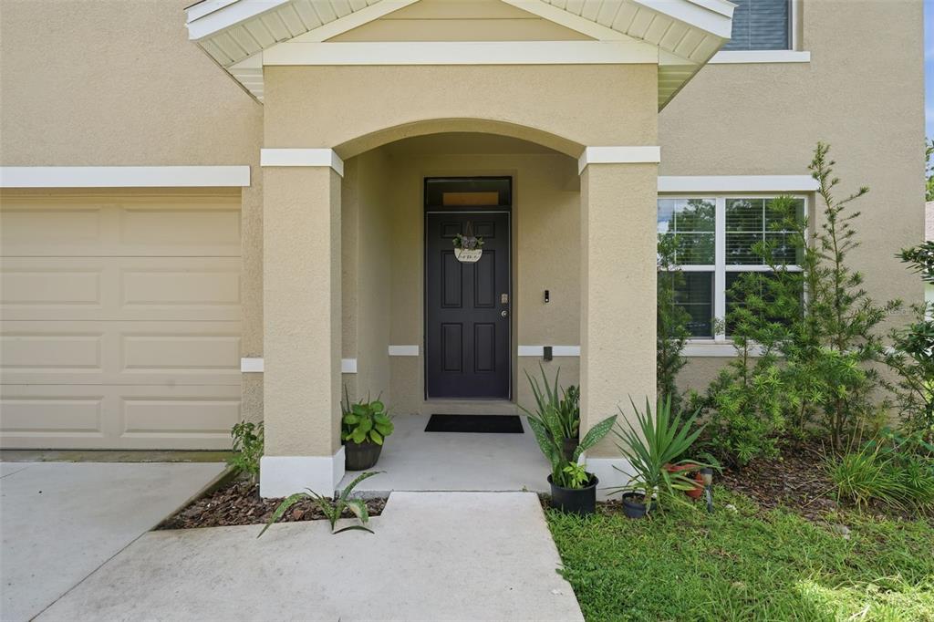 The exterior of a house features a tan stucco facade, a dark front door, and landscaping — 62 HICKORY COURSE CIRCLE, OCALA, FL