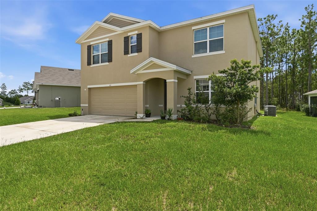 A two-story tan house with a two-car garage and a front porch sits on grass — 62 HICKORY COURSE CIRCLE, OCALA, FL