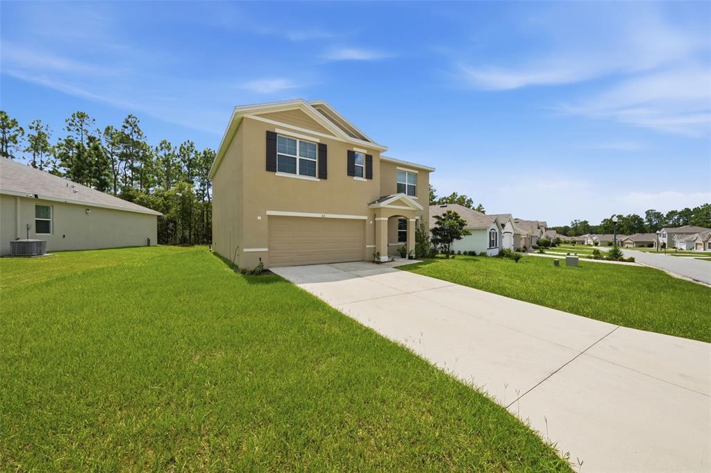 A two-story suburban house with a tan stucco exterior, a two-car garage, and a driveway — 62 HICKORY COURSE CIRCLE, OCALA, FL
