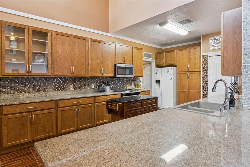 A kitchen features oak cabinets, granite countertops, a mosaic tile backsplash, and stainless steel appliances — 2606 ROYAL FERN PLACE, KISSIMMEE, FL