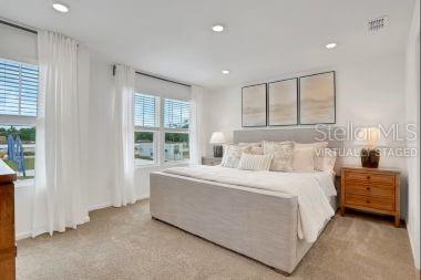 A bedroom features a large bed, a wooden nightstand, and windows with white curtains — 7646 COMMANDER LANE, JACKSONVILLE, FL