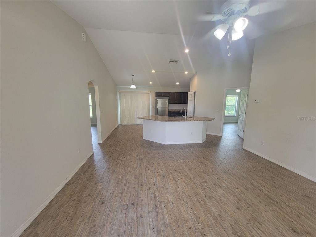 An open-concept living area features wood-look flooring, a vaulted ceiling, and a kitchen island — 42 JUNIPER LOOP CIRCLE, OCALA, FL