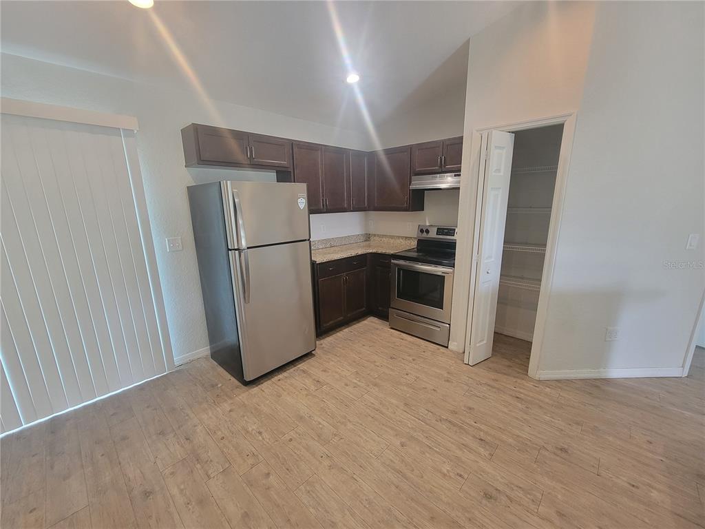 A kitchen features dark wood cabinets, stainless steel appliances, granite countertops, and light wood flooring — 42 JUNIPER LOOP CIRCLE, OCALA, FL
