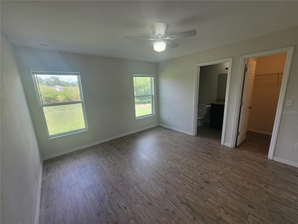 A bedroom with light gray walls, wood-look flooring, a ceiling fan, and two doorways — 42 JUNIPER LOOP CIRCLE, OCALA, FL