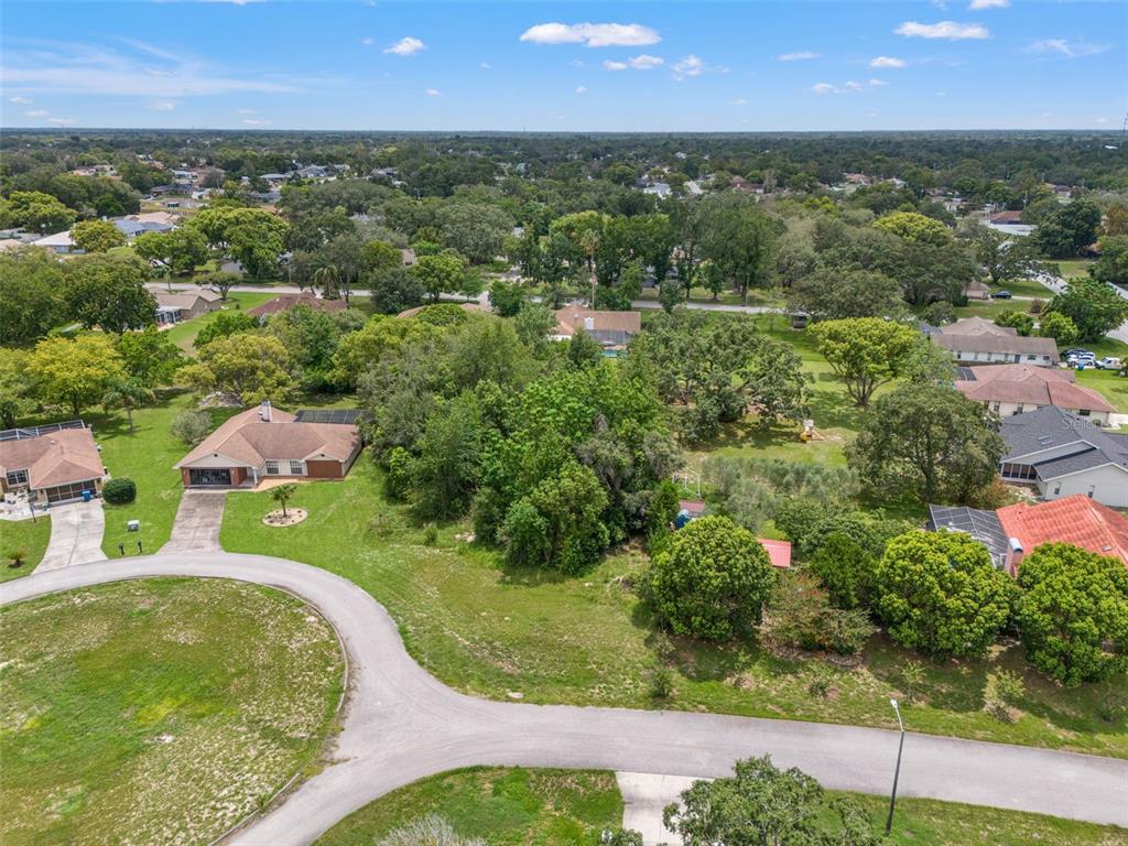 An aerial view shows a residential neighborhood with houses, driveways, and surrounding trees and lawns — NORTHWIND COURT, SPRING HILL, FL