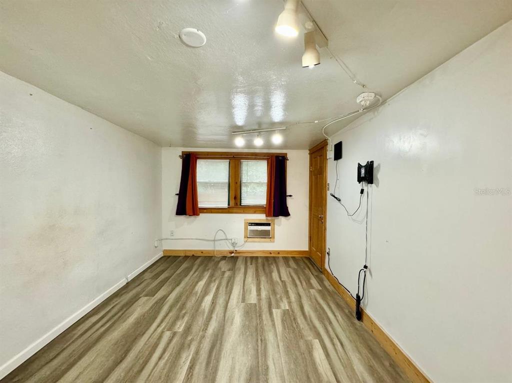 An empty room features wood-look laminate flooring, white walls, a window with curtains, and track lighting — 6601 N NAVIN AVENUE UNIT A, TAMPA, FL
