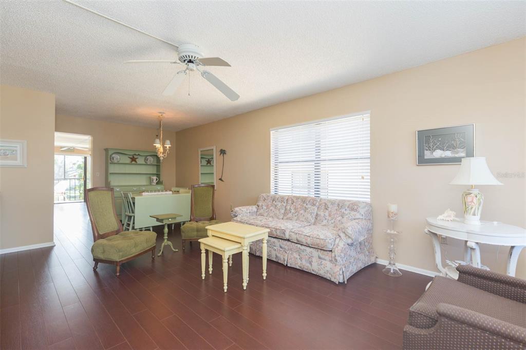 A living room features dark wood flooring, a floral sofa, and a light green dining hutch — 315 30 AVENUE W UNIT B201, BRADENTON, FL