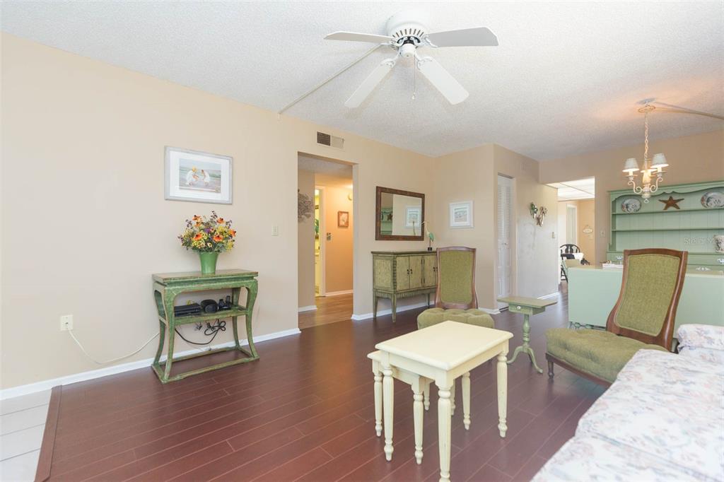 A living room with dark wood floors, a ceiling fan, and green upholstered accent chairs — 315 30 AVENUE W UNIT B201, BRADENTON, FL