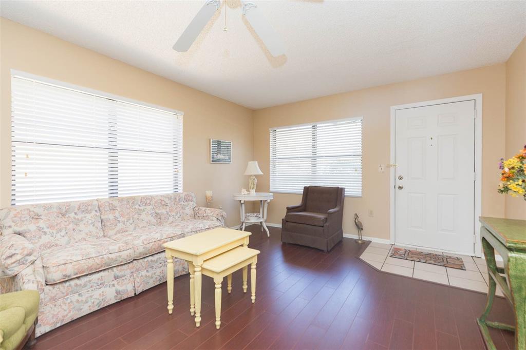 A living room features floral sofa, brown armchair, nested tables, and wood-look flooring — 315 30 AVENUE W UNIT B201, BRADENTON, FL