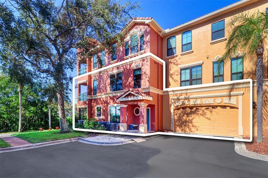 A three-story townhouse exterior with a red stucco facade, a garage, and a front entrance — 2757 VIA CIPRIANI UNIT 1114A, CLEARWATER, FL