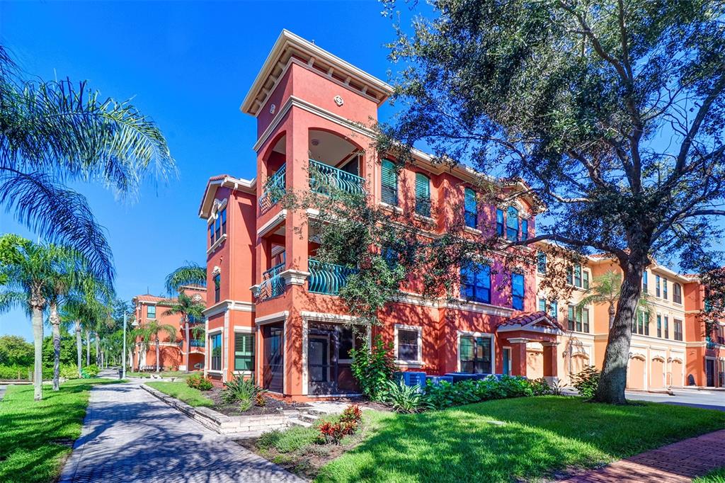 A three-story orange apartment building with balconies and palm trees under a clear blue sky — 2757 VIA CIPRIANI UNIT 1114A, CLEARWATER, FL