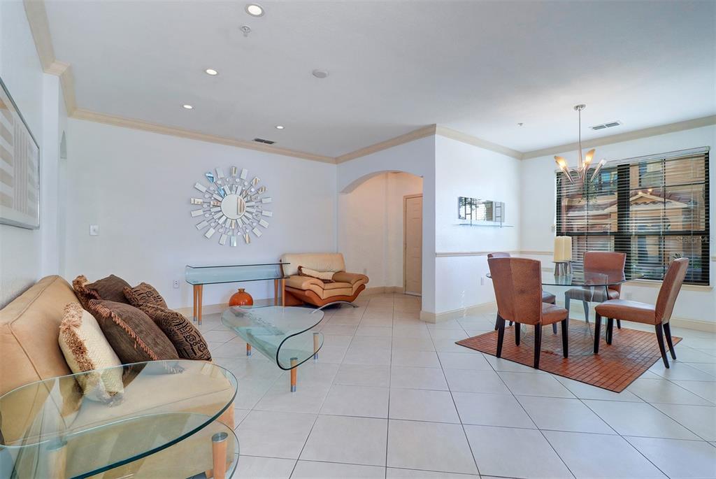 A living and dining area with tile floors, a glass coffee table, and a sunburst mirror — 2757 VIA CIPRIANI UNIT 1114A, CLEARWATER, FL