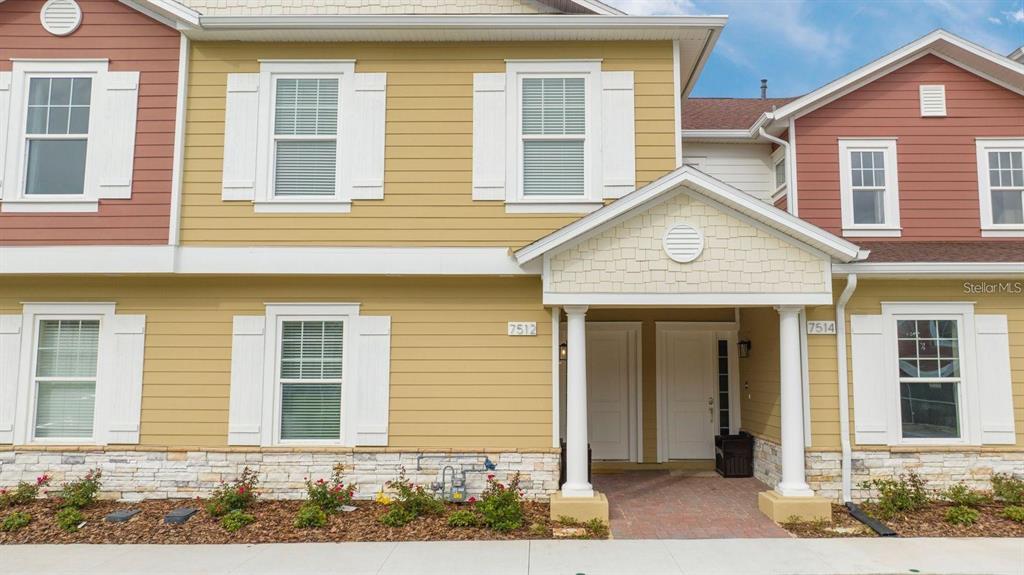 A two-story townhouse exterior features yellow siding, white shutters, and a covered front entryway — 7512 SUNFLOWER CIRCLE, KISSIMMEE, FL