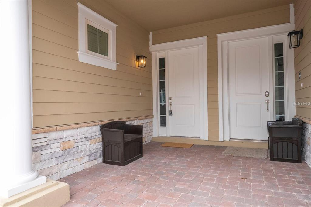 A covered porch features a brick floor, stone siding, two white doors, and two chairs — 7512 SUNFLOWER CIRCLE, KISSIMMEE, FL