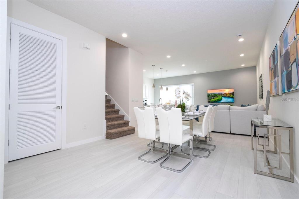 A bright, open-concept dining area features white chairs, a glass table, and light wood flooring — 7512 SUNFLOWER CIRCLE, KISSIMMEE, FL