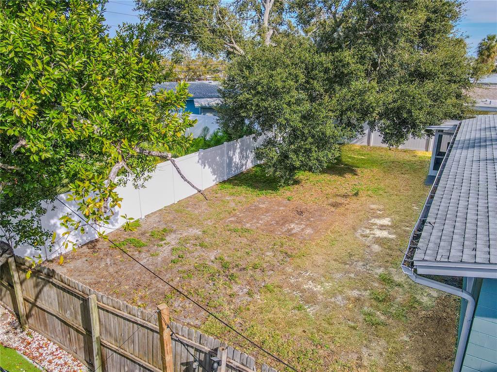 A backyard with a patchy lawn, a large tree, and white vinyl fencing — 11615 PARK BOULEVARD, SEMINOLE, FL