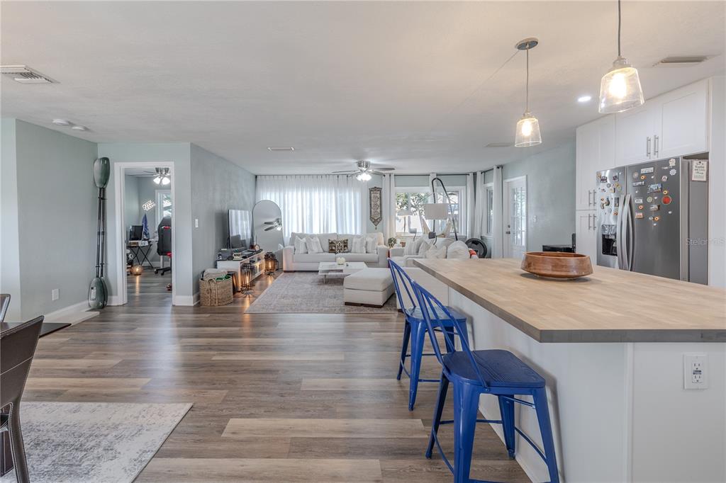 An open-concept kitchen and living area features wood-look flooring, blue bar stools, and white cabinetry — 11615 PARK BOULEVARD, SEMINOLE, FL