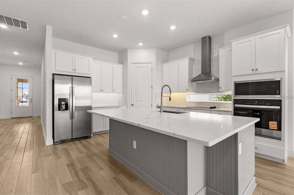 A modern kitchen features white cabinetry, a gray island with a quartz countertop, and stainless appliances — 9930 BALLAST DRIVE, ORLANDO, FL