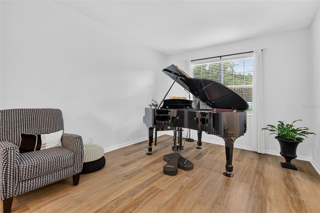 A room with wood-look flooring features a black grand piano and a patterned armchair — 1450 OSPREY RIDGE DRIVE, EUSTIS, FL
