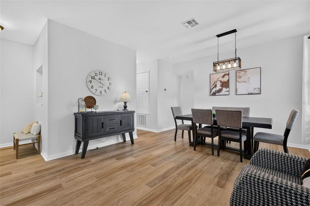A dining room features wood-look flooring, a dark sideboard, a dining table with chairs, and wall art — 1450 OSPREY RIDGE DRIVE, EUSTIS, FL