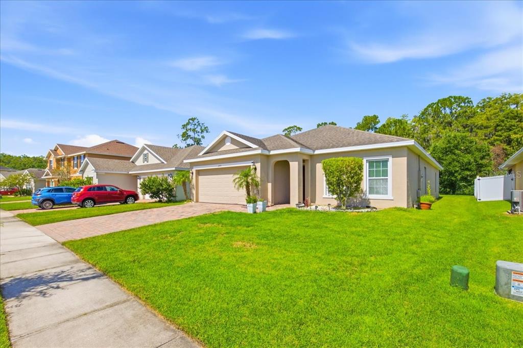A single-story suburban house with a tan exterior, a two-car garage, and a green lawn — 2414 ADDISON CREEK DRIVE, KISSIMMEE, FL