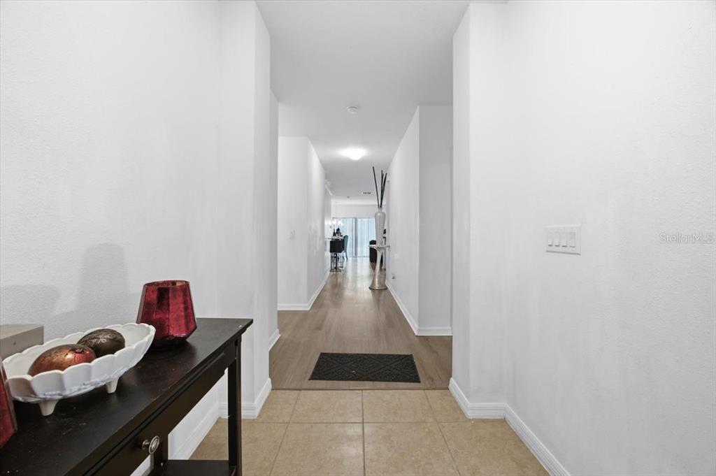 A hallway with tile flooring transitions to wood-look flooring, leading toward an open living area — 2414 ADDISON CREEK DRIVE, KISSIMMEE, FL