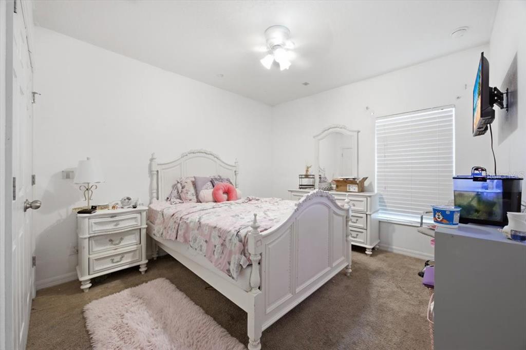 A bedroom features a white bed frame, a matching nightstand, a dresser, and carpeted flooring — 2414 ADDISON CREEK DRIVE, KISSIMMEE, FL