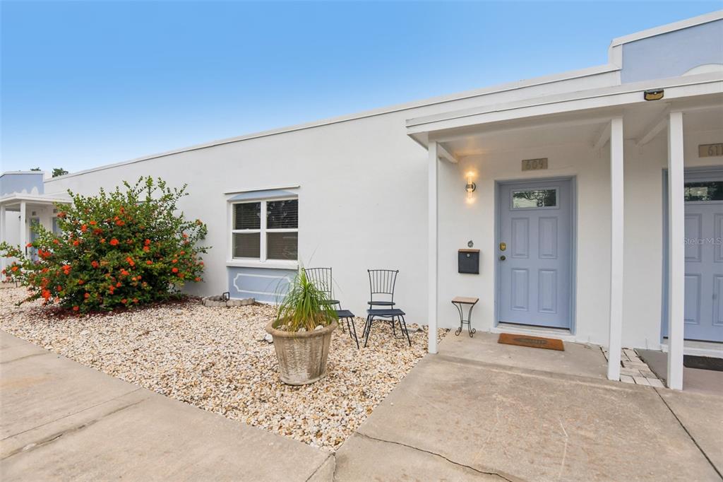 The exterior of a white building features a light blue door, gravel landscaping, and chairs — 609 WESTWINDS DRIVE UNIT 4, PALM HARBOR, FL
