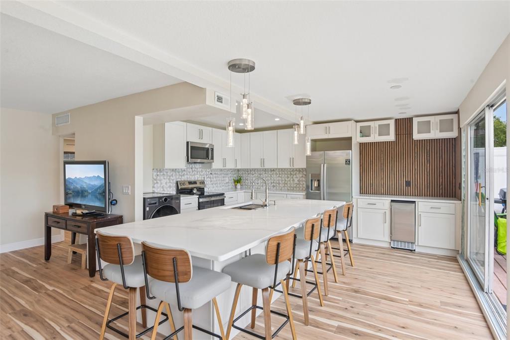 A modern kitchen features a large white island, wood-toned bar stools, and light wood flooring — 609 WESTWINDS DRIVE UNIT 4, PALM HARBOR, FL