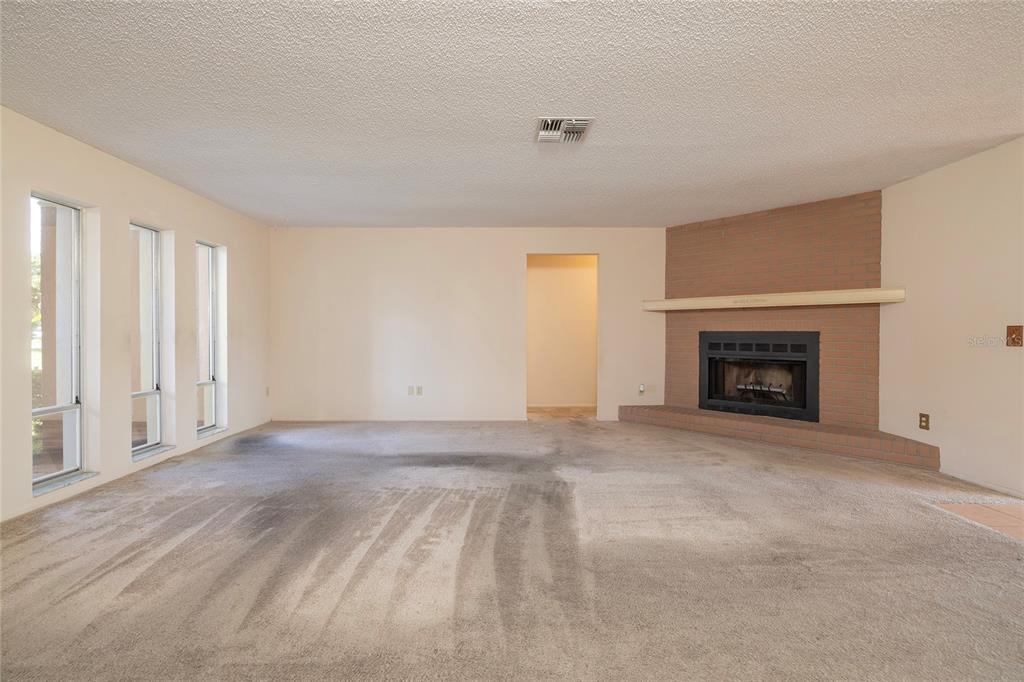 A living room with beige carpet, light walls, and a corner brick fireplace — 6355 102ND TERRACE N, PINELLAS PARK, FL