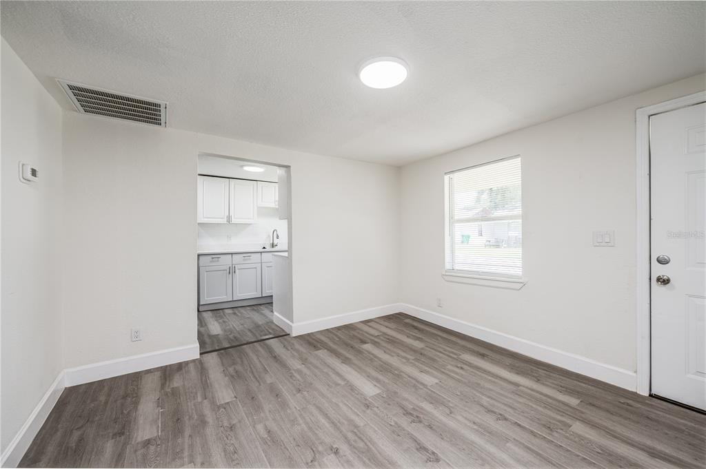 A room with gray wood-look flooring, white walls, a window, and an opening to a kitchen — 1422 BASIN STREET, WINTER GARDEN, FL