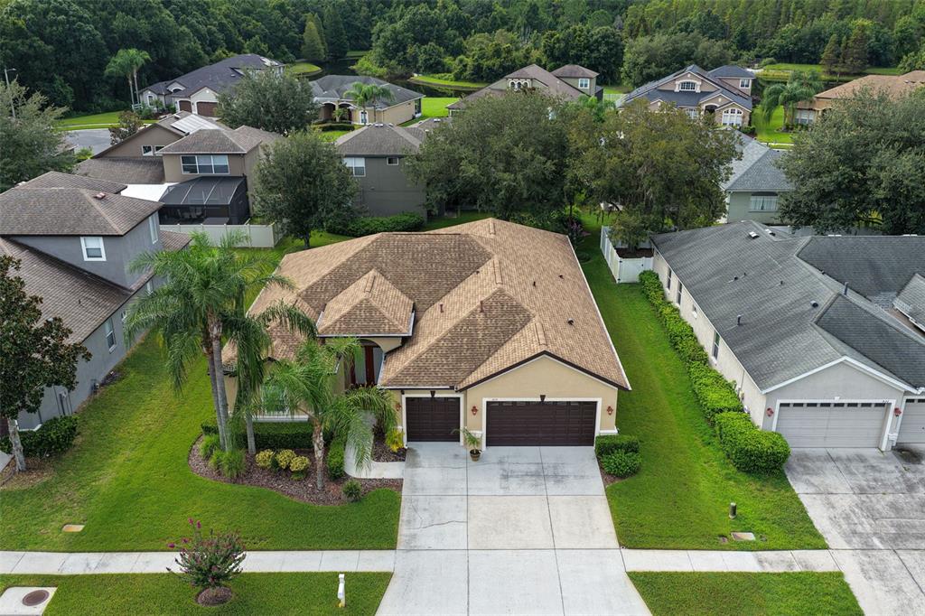 An aerial view shows a tan single-story house with a brown roof and three-car garage — 1430 BEACONSFIELD DRIVE, WESLEY CHAPEL, FL