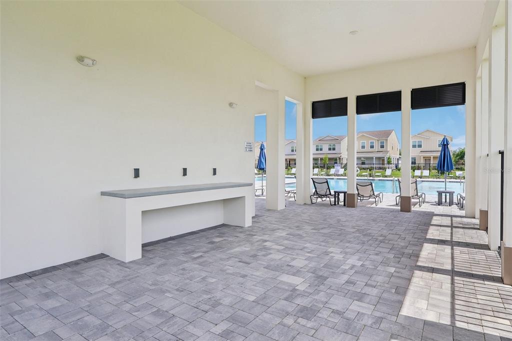 A covered patio features a built-in counter, paver flooring, and a view of a swimming pool — 1813 LATTICE WAY, ST CLOUD, FL