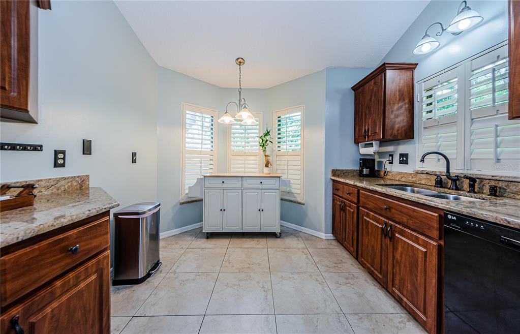 A kitchen features wood cabinets, granite countertops, a central island, and tile flooring — 3647 MUIRFIELD COURT, NEW PORT RICHEY, FL