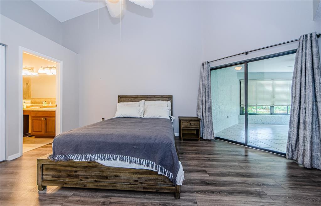 A bedroom with wood-look flooring, a wooden bed frame, and sliding glass doors to a patio — 3647 MUIRFIELD COURT, NEW PORT RICHEY, FL