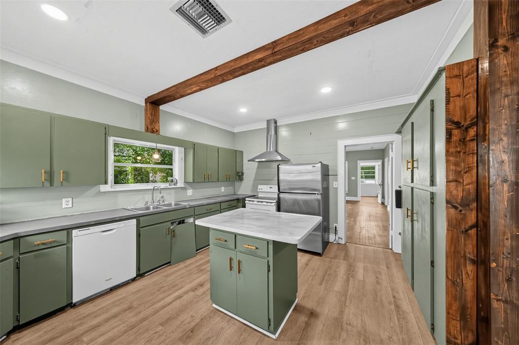 A kitchen features sage green cabinets, a white island, stainless steel appliances, and wood beams — 1203 KING AVENUE, LAKELAND, FL