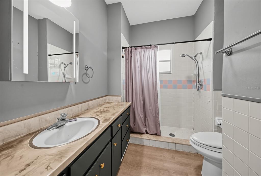 A bathroom features a dark vanity with a light countertop, a toilet, and a shower stall — 1203 KING AVENUE, LAKELAND, FL