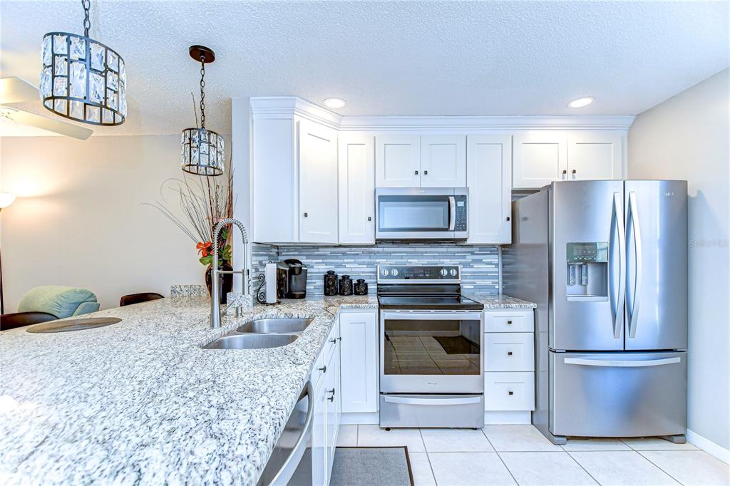 A kitchen features white cabinets, granite countertops, stainless steel appliances, and a tiled backsplash — 13870 OAKWOOD LANE, SEMINOLE, FL