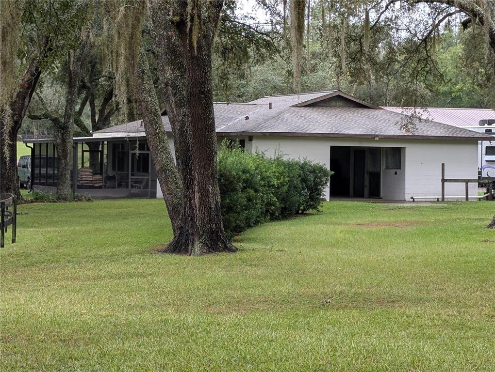 A white house with a screened porch sits on a large, tree-shaded grassy lot — 10871 SE COUNTY ROAD 326, MORRISTON, FL