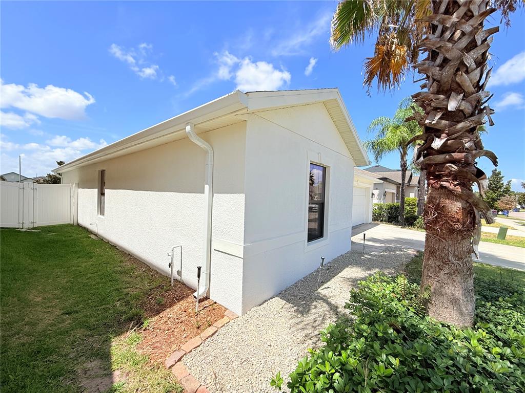 The exterior side of a white stucco house features a window, downspout, and gravel landscaping — 14323 HADDON MIST DRIVE, WIMAUMA, FL
