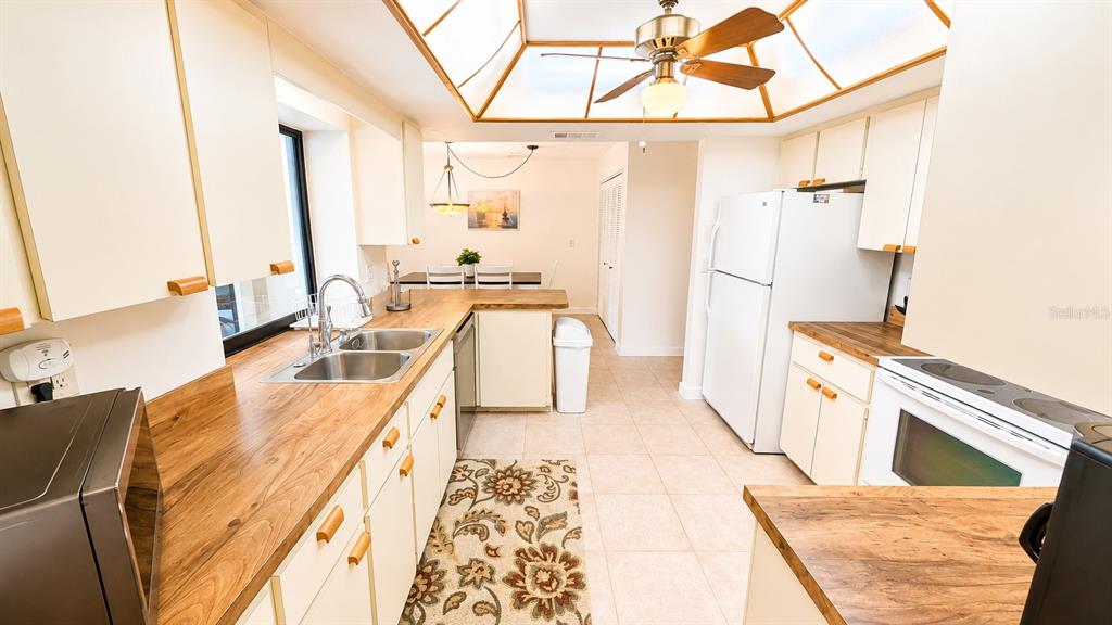 A kitchen with light-colored cabinets, wood countertops, a breakfast bar with stools, and tile flooring — 1526 GEORGETOWNE LANE, SARASOTA, FL