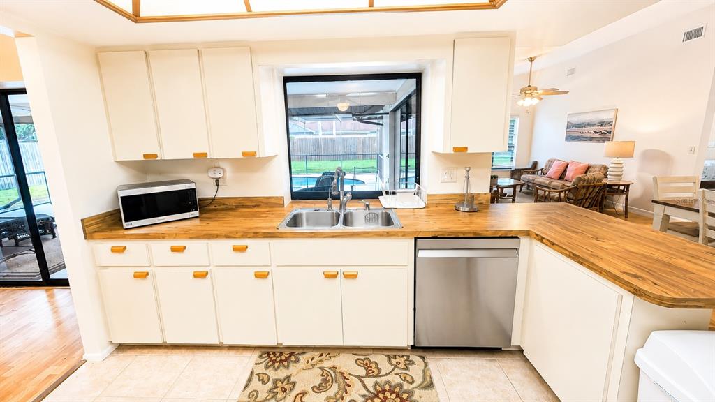 A kitchen features a wooden breakfast bar with two stools, white cabinets, and tile flooring — 1526 GEORGETOWNE LANE, SARASOTA, FL