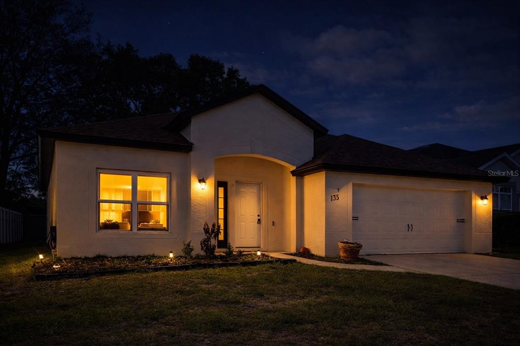 A single-story house with a white stucco exterior and a two-car garage at night — 133 JAYBEE AVENUE, DAVENPORT, FL